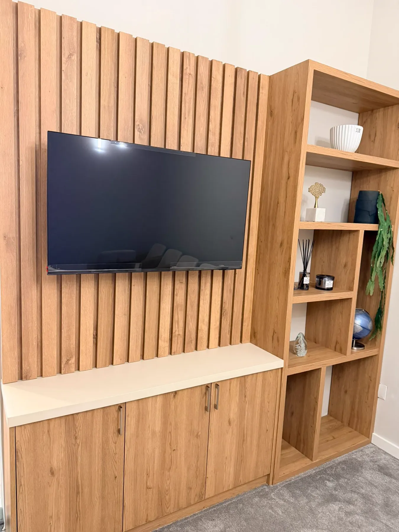 Mur à tasseaux en bois avec meuble TV et bibliothèque sur mesure, réalisé par Mestria